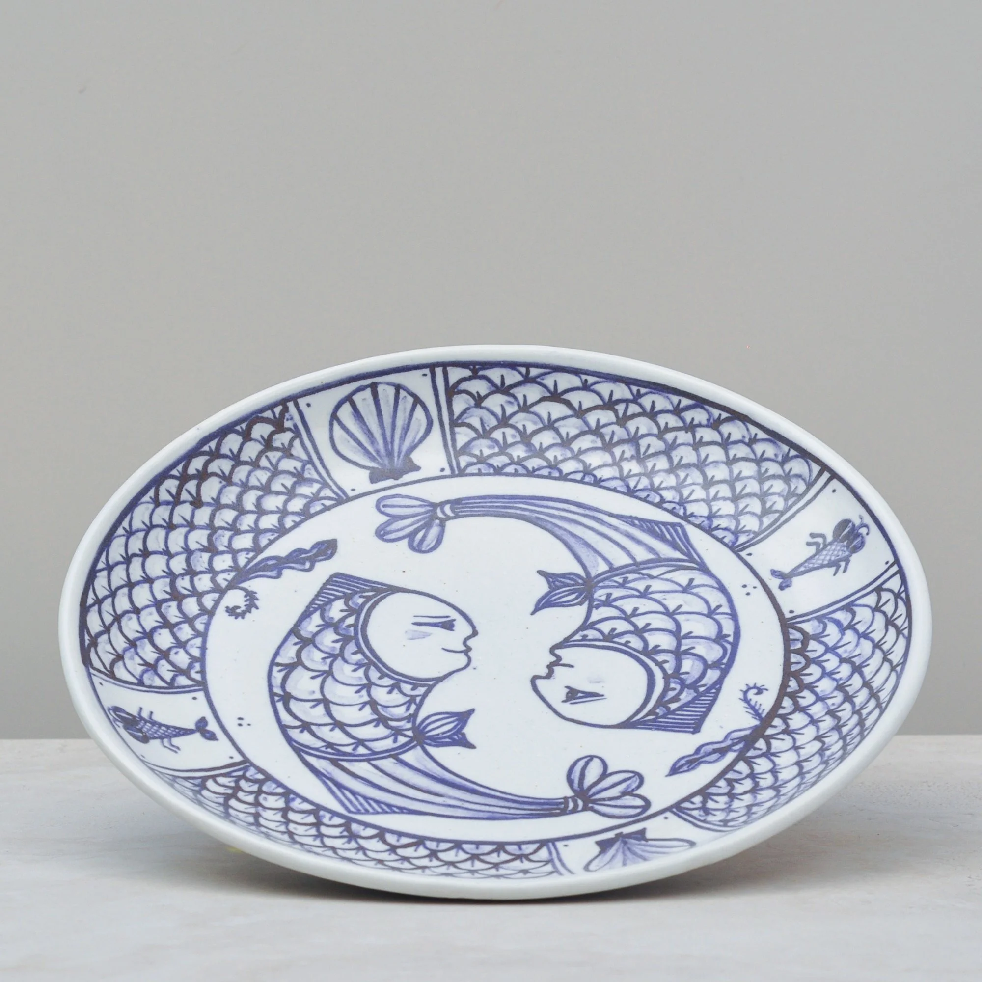 Vintage blue and white ceramic plate with a stylised fish and geometric border pattern.