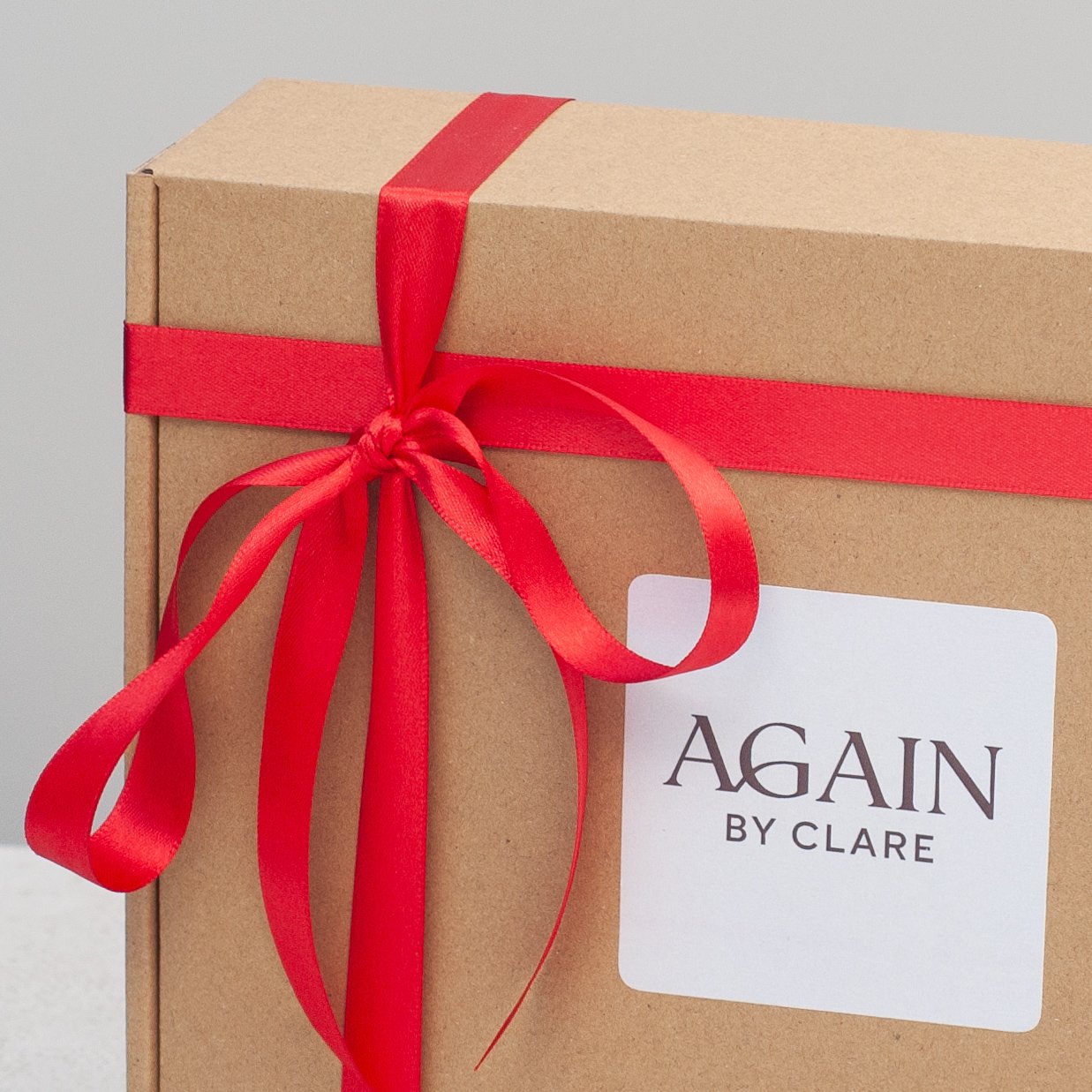 Gift box with red ribbon and an Again by Clare label — meaningful gift presentation.