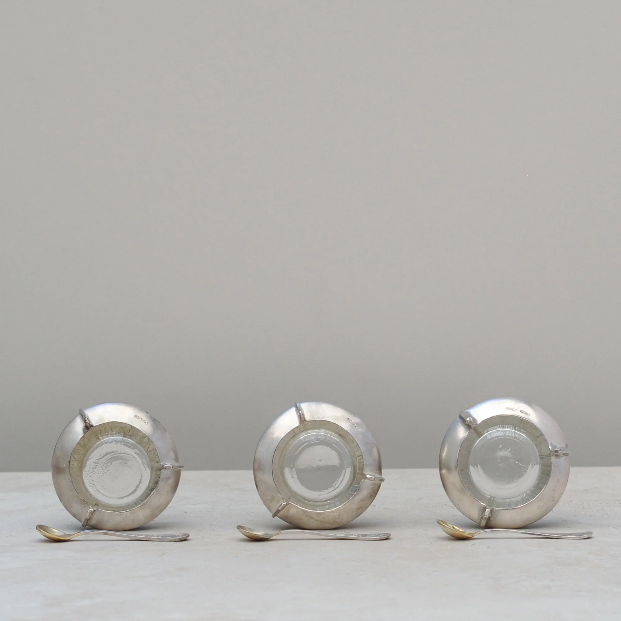 Underside view of three mid-century silver-plated cloisonné salt cellars showing maker’s marks and bases.