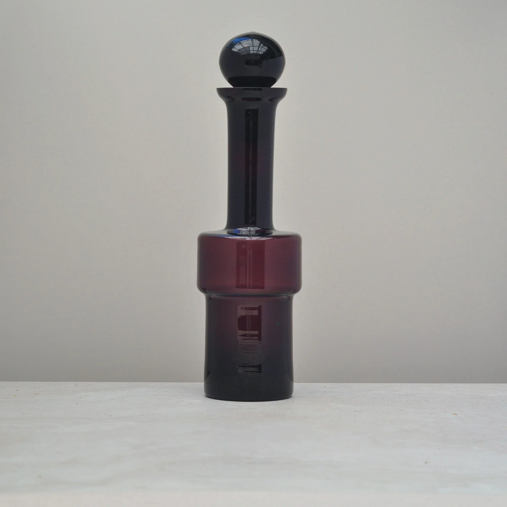 “Front view of a mid-century aubergine glass decanter with stopper, showing its tall sculptural silhouette.