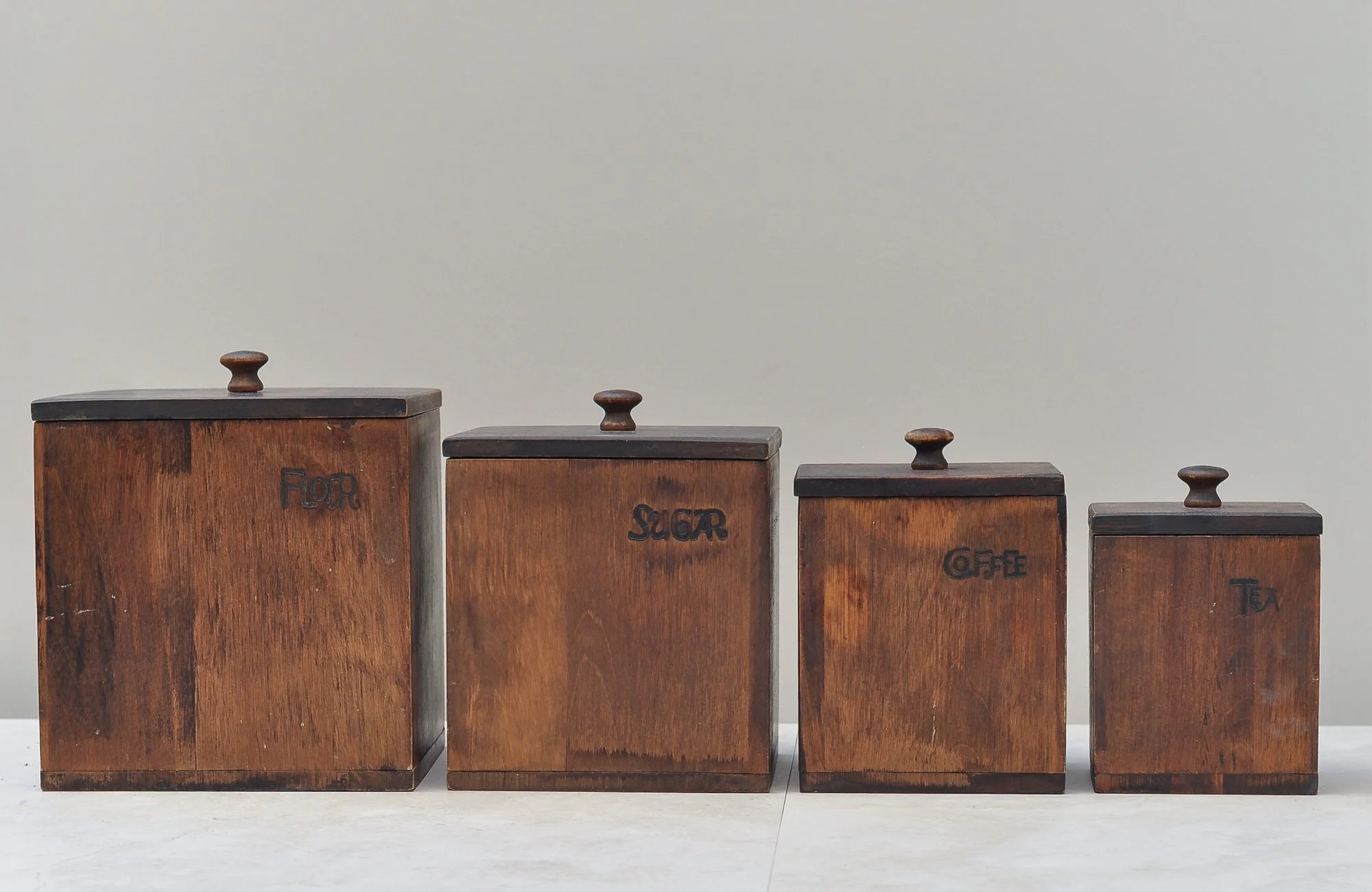 Front view of a vintage wooden canister set for tea, coffee, sugar and spice, displayed with matching lids.