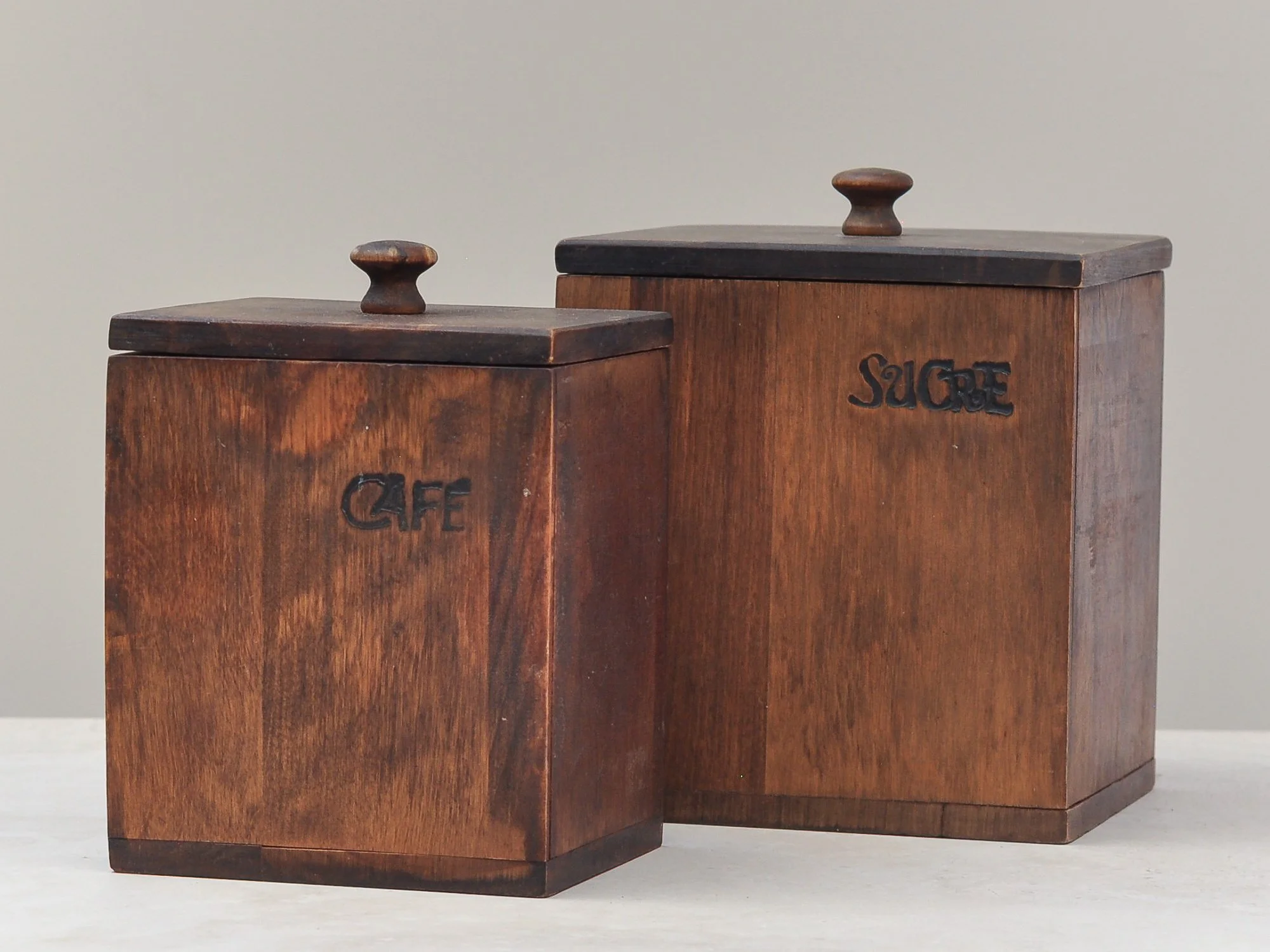 Vintage wooden tea, coffee and sugar canisters arranged together, displaying rich tone and aged texture.