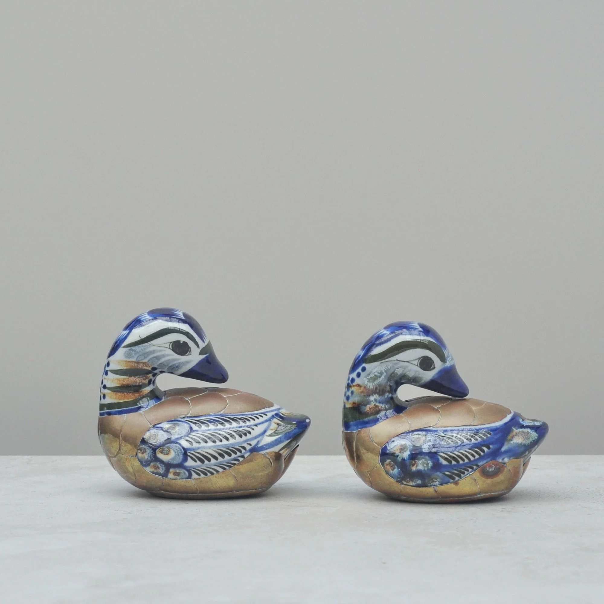 Hand-painted Mexican Tonalá duck figurines with brass bases, shown from a three-quarter angle highlighting their expressive patterning.
