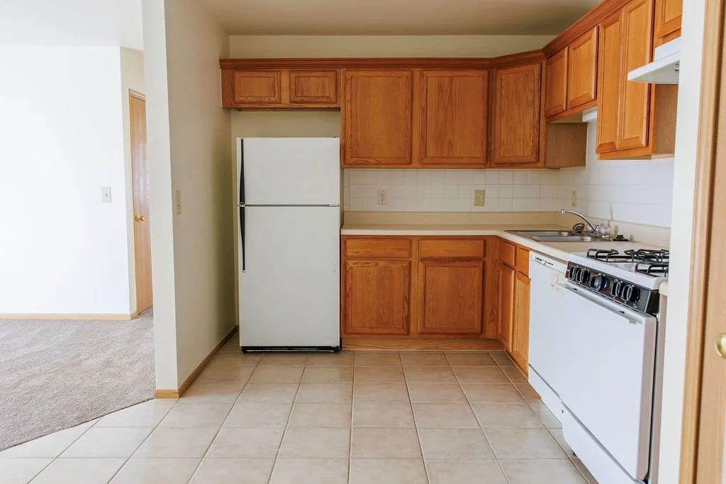 Kitchen with wooden cabinets, a white refrigerator, a small sink, and a white stove with four burners.