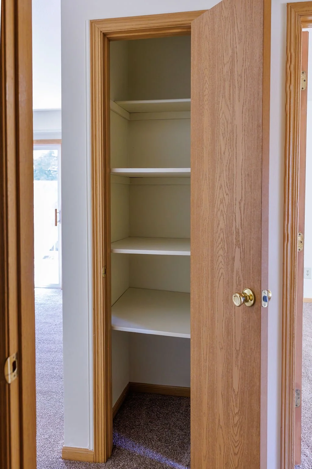 Empty wooden closet with four white shelves inside, open door revealing the closet interior.