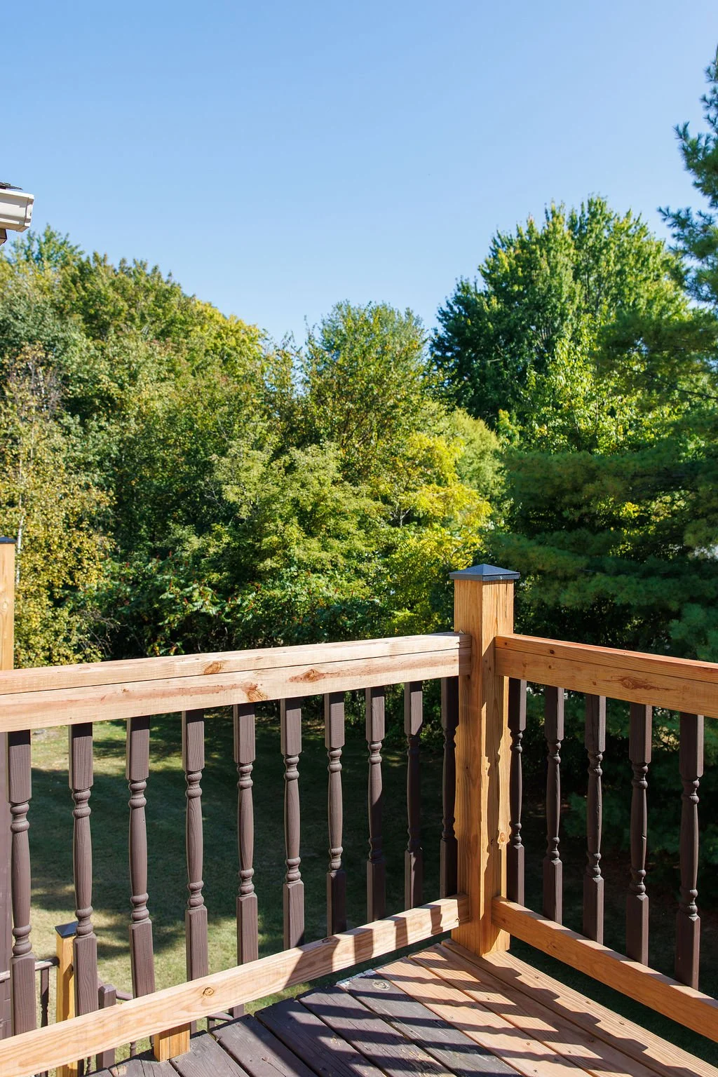 A wooden balcony railing overlooking a lush green treetop landscape under a clear blue sky.
