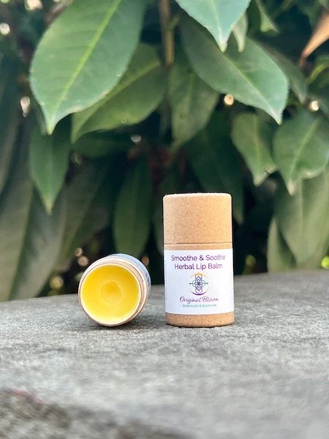A herbal lip balm tube with a yellow balm inside, placed on a wooden surface with green foliage in the background.