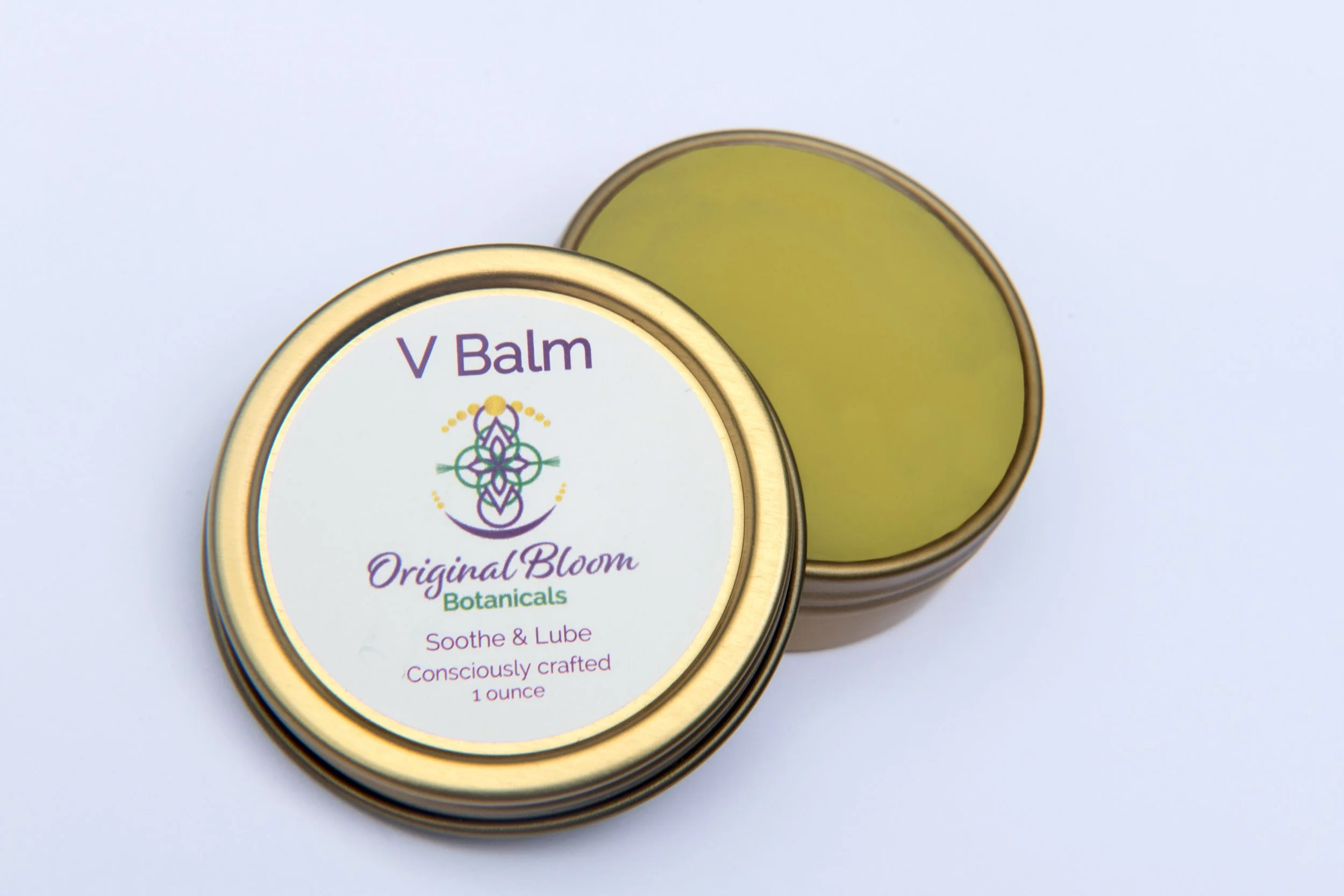 Open tin container of vegan balm labeled 'V Balm' from Original Bloom Botanicals, designed to soothe and lubricate, with the balm inside being yellow.