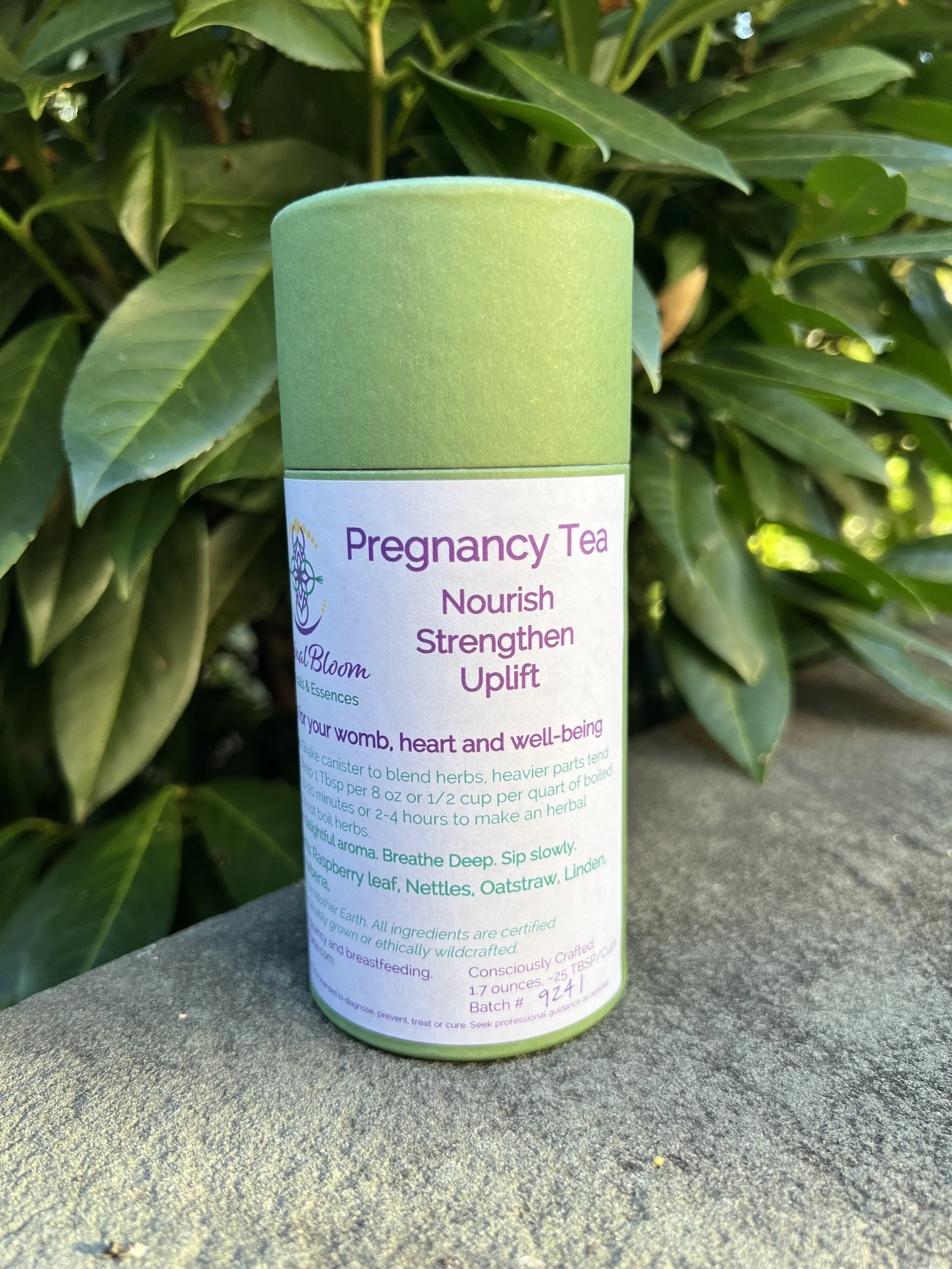 A green cylindrical container of Pregnancy Tea placed outdoors on a stone surface, with green foliage in the background.