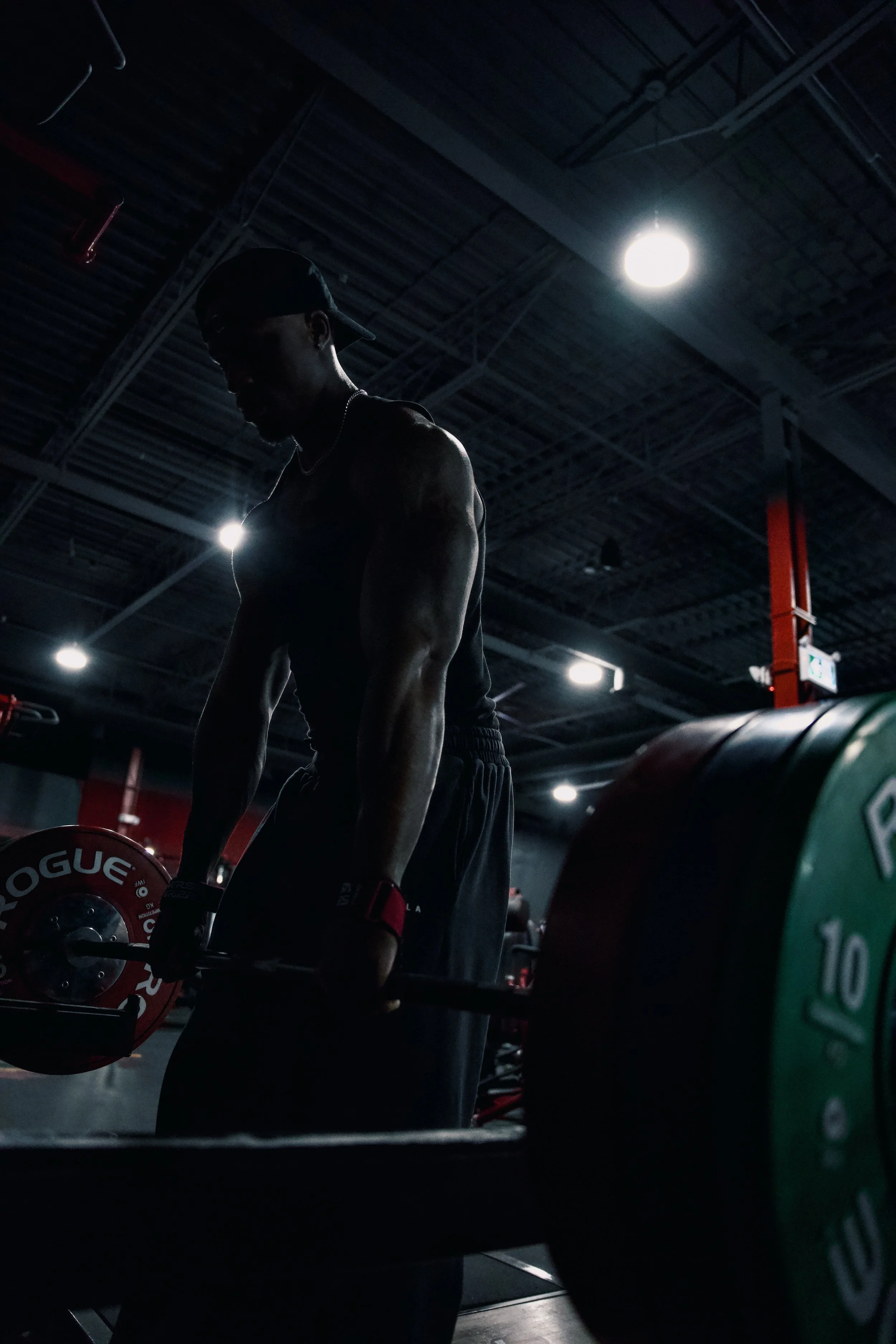 A person lifting a barbell with weights in a dark gym.