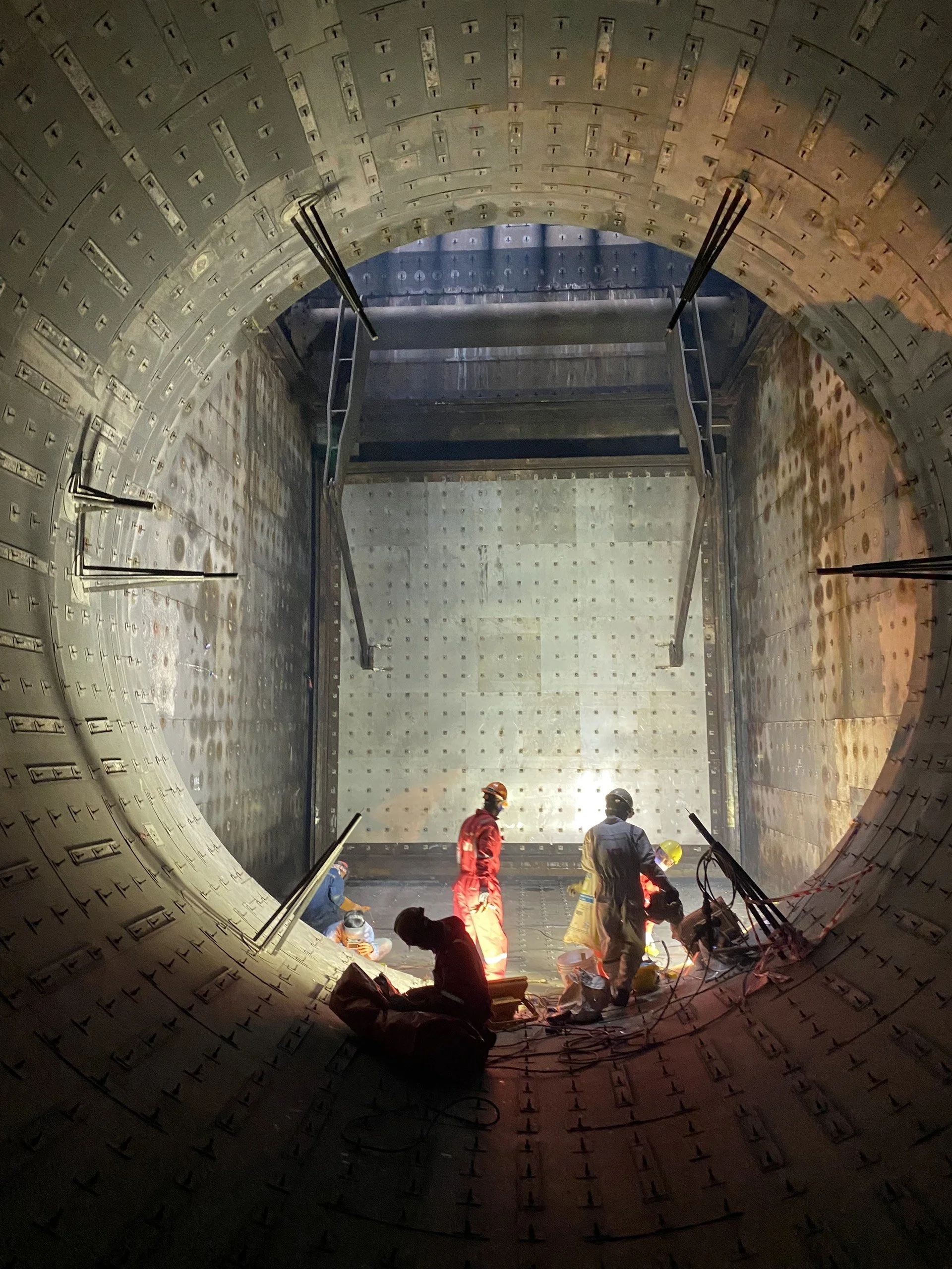 A worker in protective gear operating a machine inside a large, deep, concrete-lined tunnel or trench.