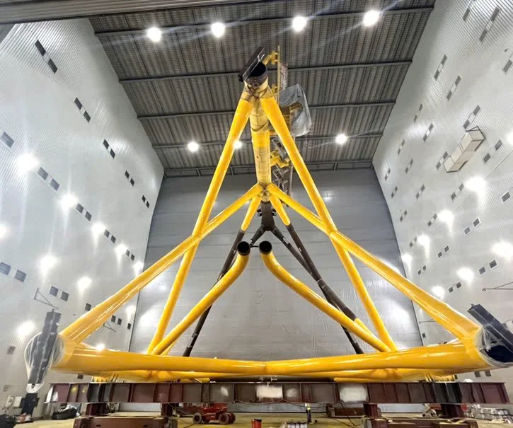 Large yellow and black telescope assembly in a spacious warehouse or hangar.