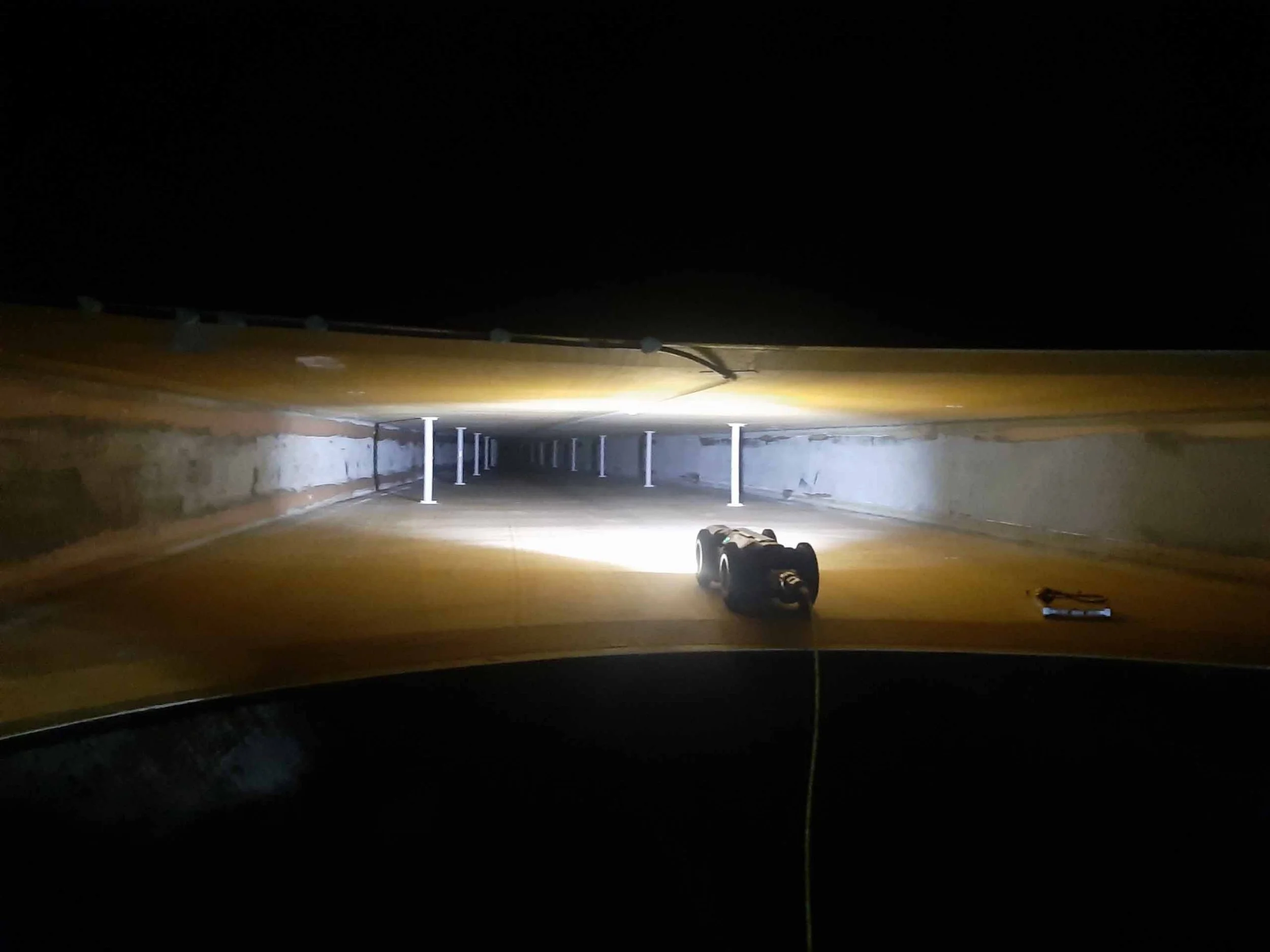 View of a tunnel with artificial lighting, supported by metal poles, and a portable work light on the ground.
