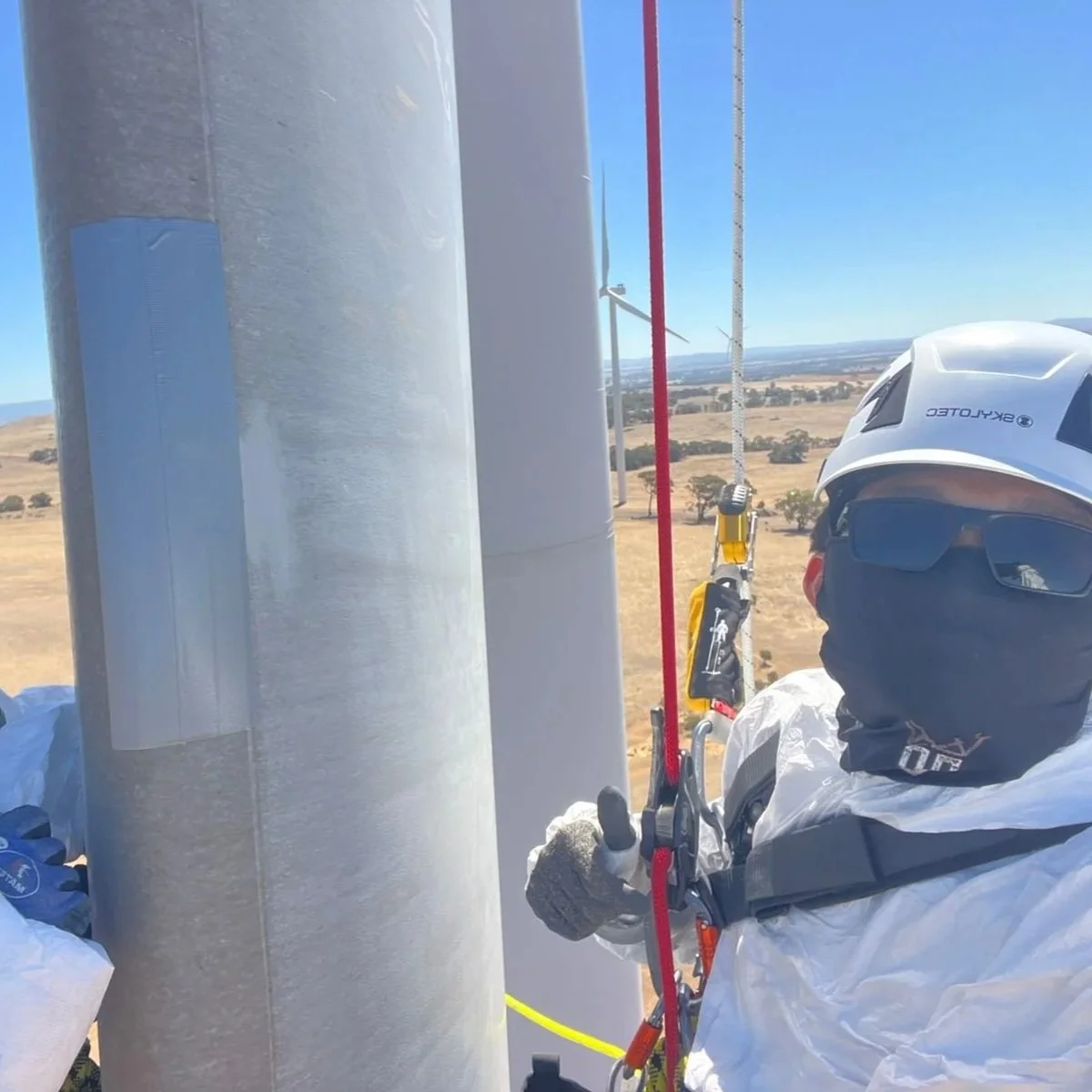 A worker in safety gear inspecting a large industrial storage tank in a factory or manufacturing facility.