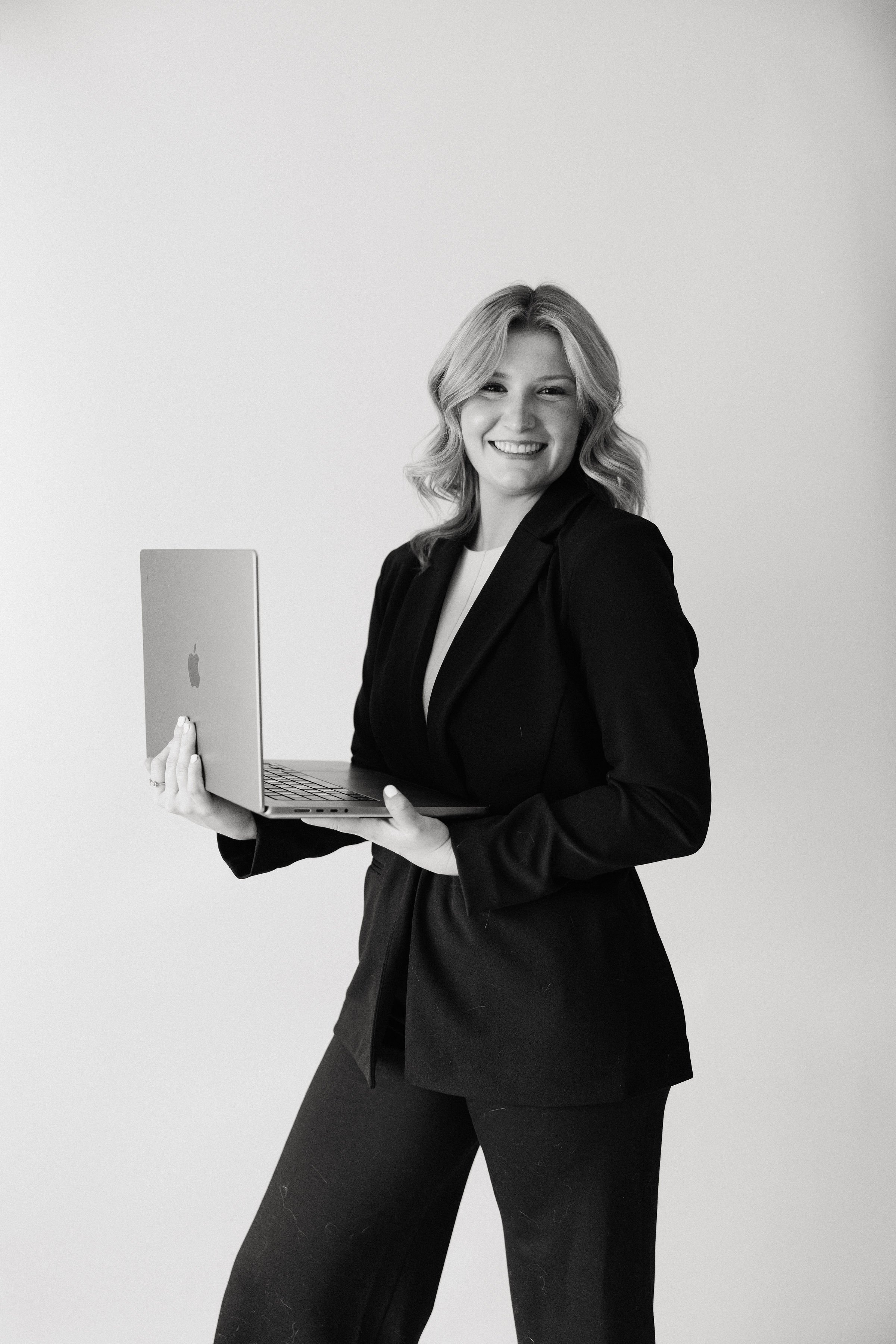 A woman in business attire smiling and holding an open laptop.