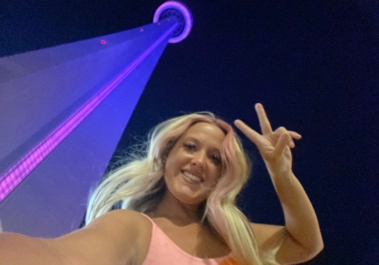 Woman taking a selfie at night with the illuminated purple CN Tower in Toronto in the background.