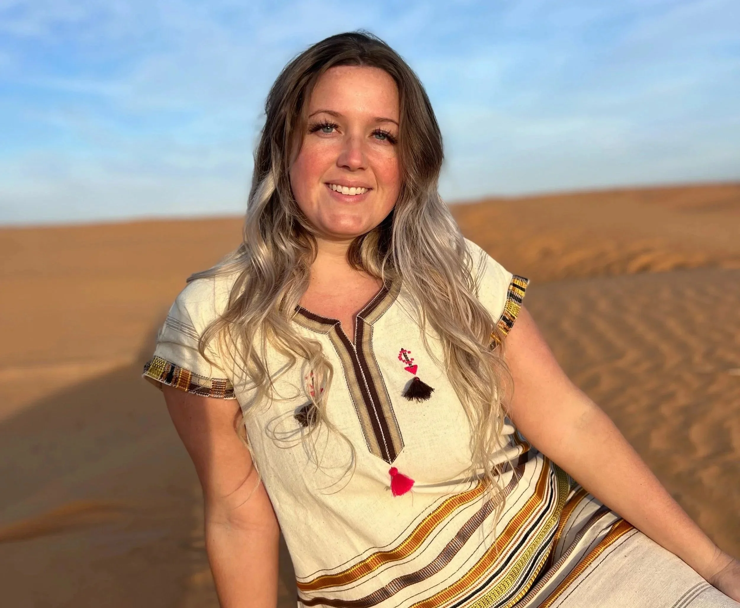 A young woman sitting on the dunes of the Sahara Desert in Tunisia, wearing a traditional Tunisian dress.