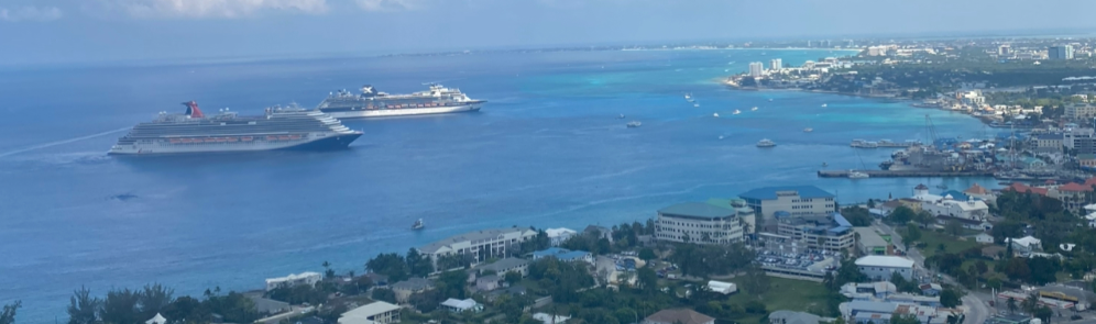 Aerial view of the crystal-blue waters of the Cayman Islands with two large cruise ships anchored offshore.