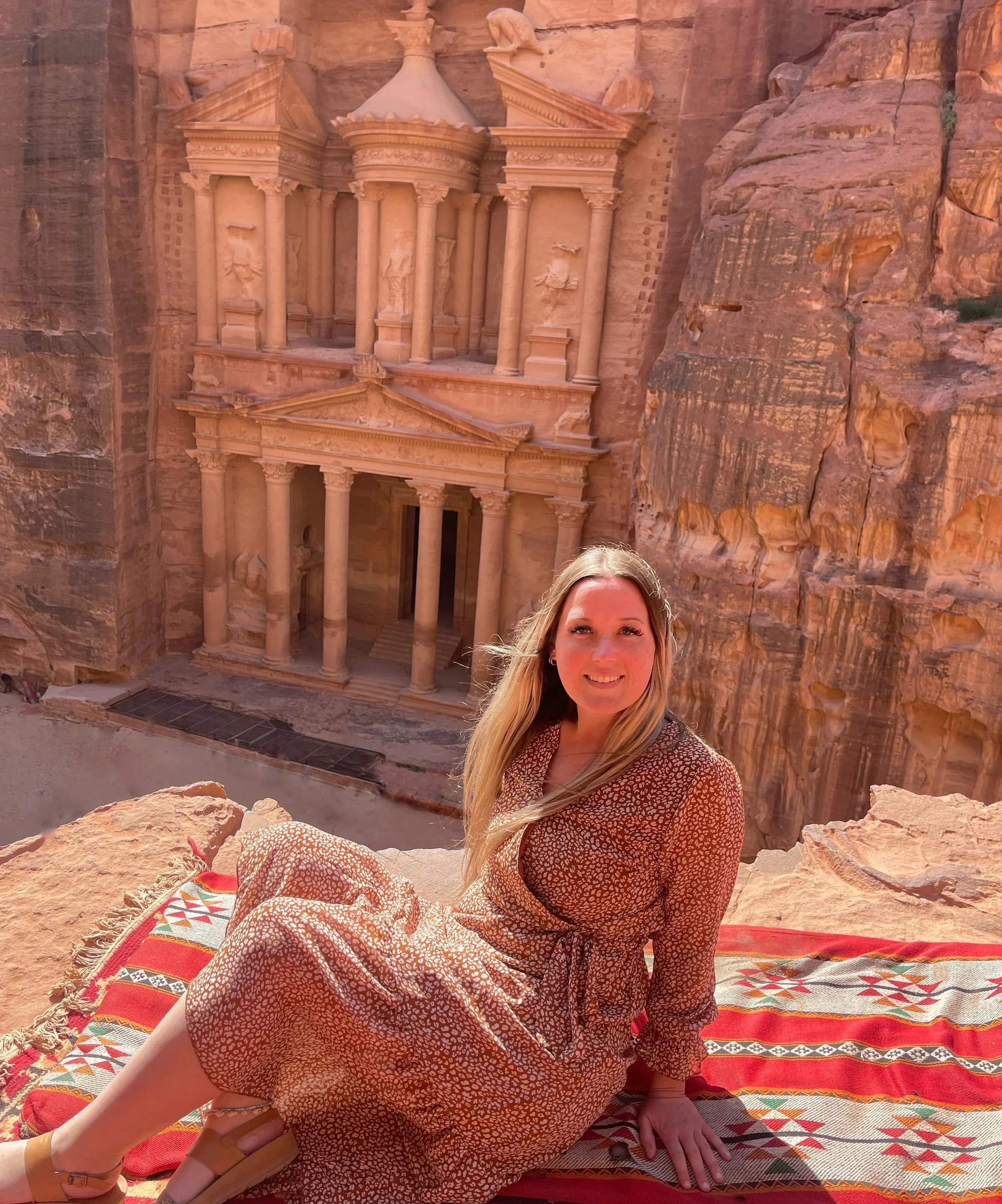 Woman smiling sitting on a ledge overlooking the Treasury at Petra in Jordan