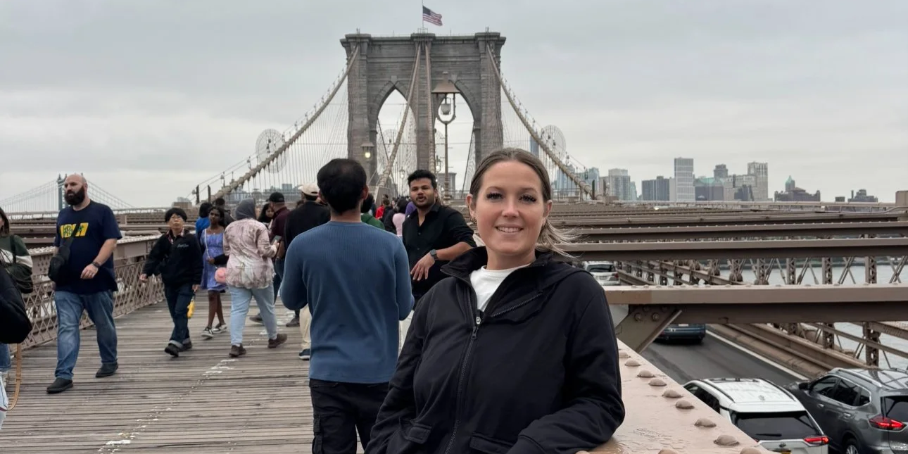 A girl smiling while standing in front of the Brooklyn Bridge in New York City.