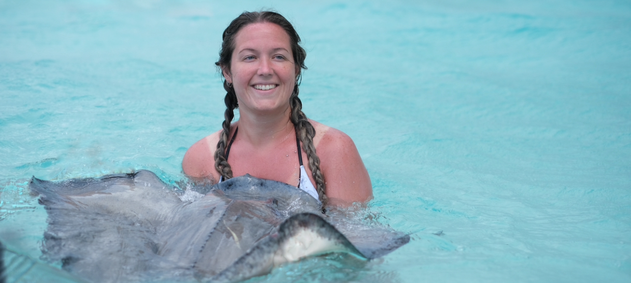 A woman smiling while gently holding a stingray in clear, shallow water.