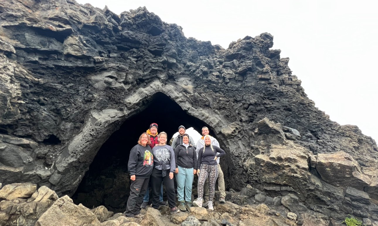 People standing in front of a large lava rock opening at Dimmuborgir Lava Formations in Iceland.