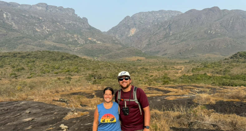 A couple hiking on trails at Santuário do Caraça in Brazil, with mountains and scenic landscape visible in the background.