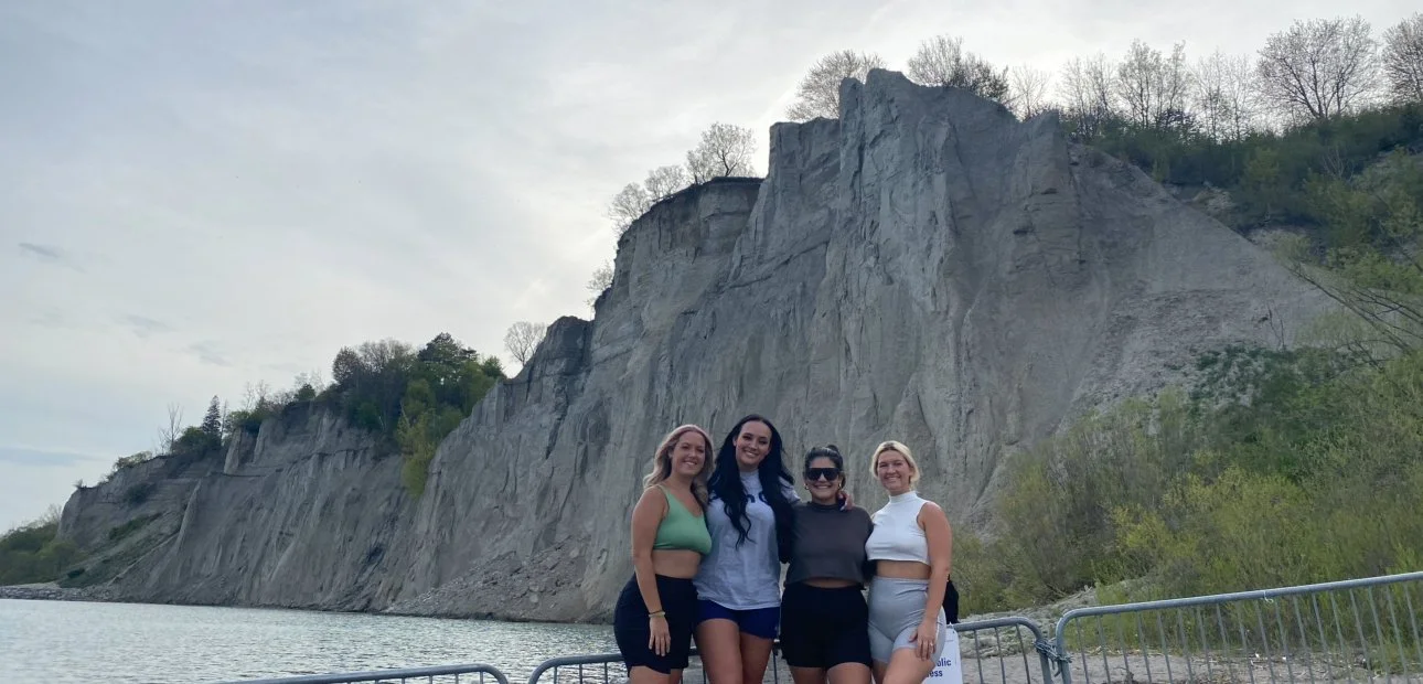 Four girls smiling and posing in front of the scenic Scarborough Bluffs cliffs and Lake Ontario shoreline.
