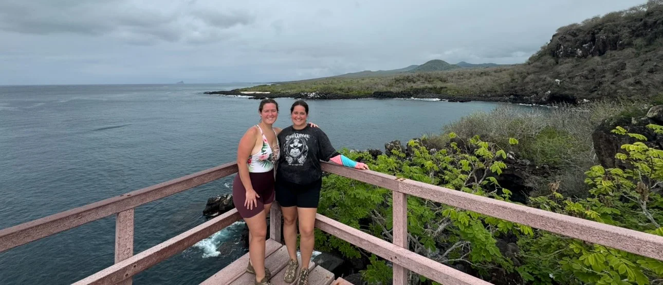 Two women standing at Cerro Tijeretas in the Galápagos Islands, overlooking the ocean and coastal cliffs.