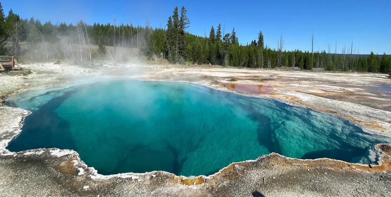A hot spring with steam rising from the Abyss Pool in Yellowstone National Park, surrounded by rocky terrain and vibrant mineral deposits.