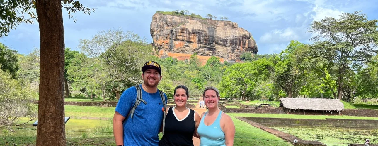 Three people posing in front of Sigiriya Rock Fortress in Sri Lanka.