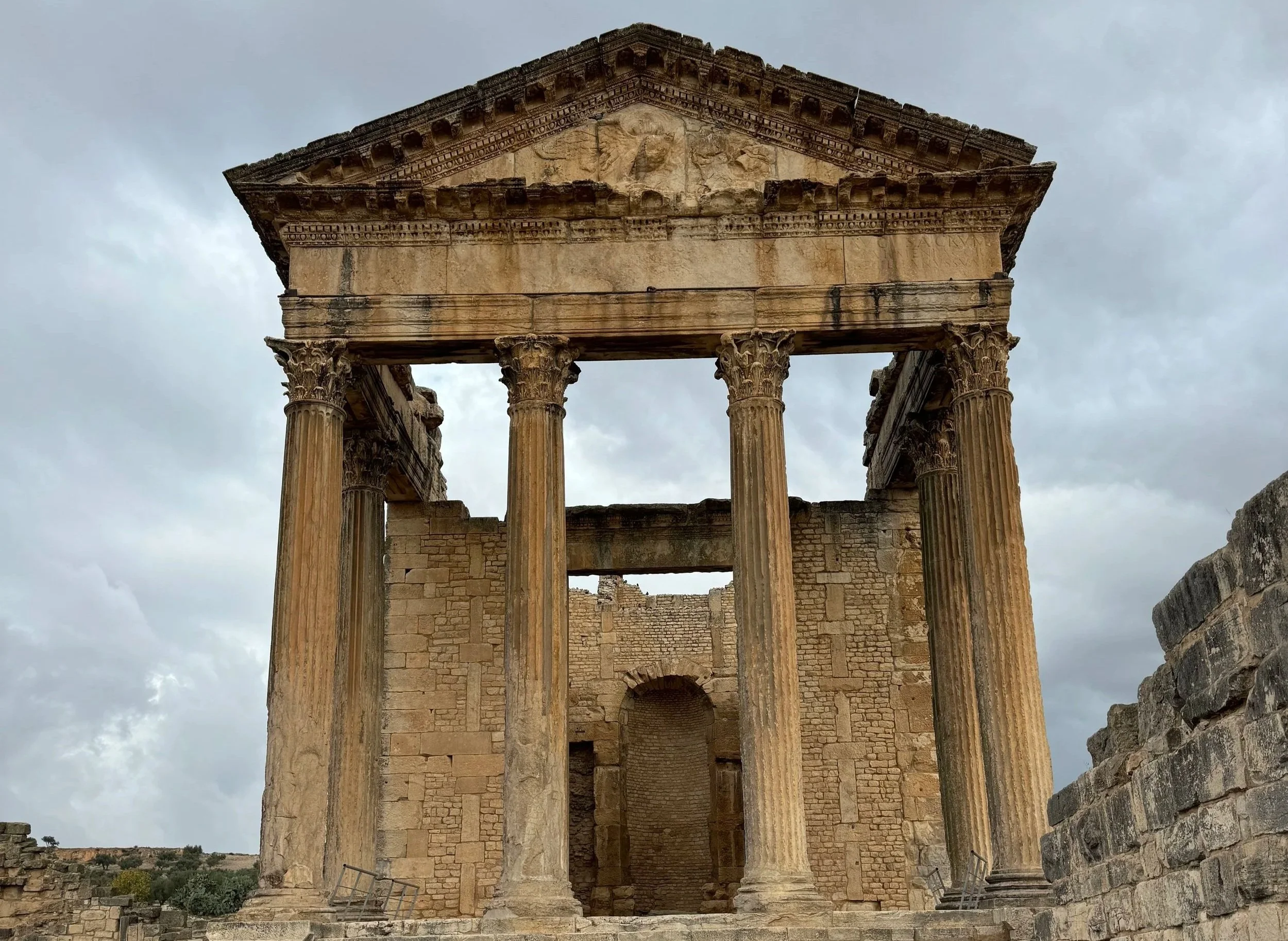 Ancient Roman ruins at Dougga in Tunisia, showcasing stone columns, arches, and archaeological structures under a clear sky.