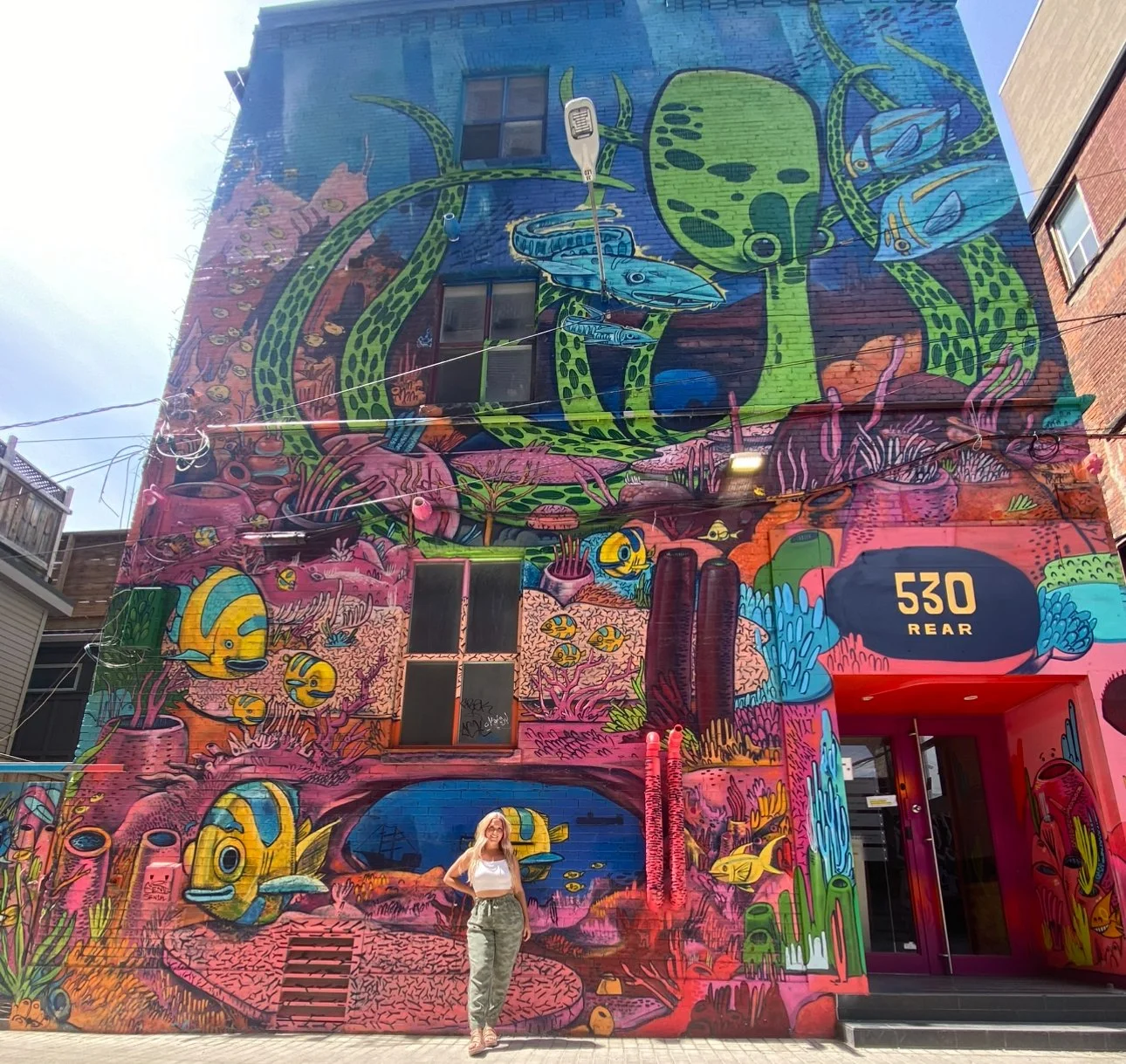 Woman standing in front of a building in Graffiti Alley featuring a vibrant, colorful ocean-themed mural.