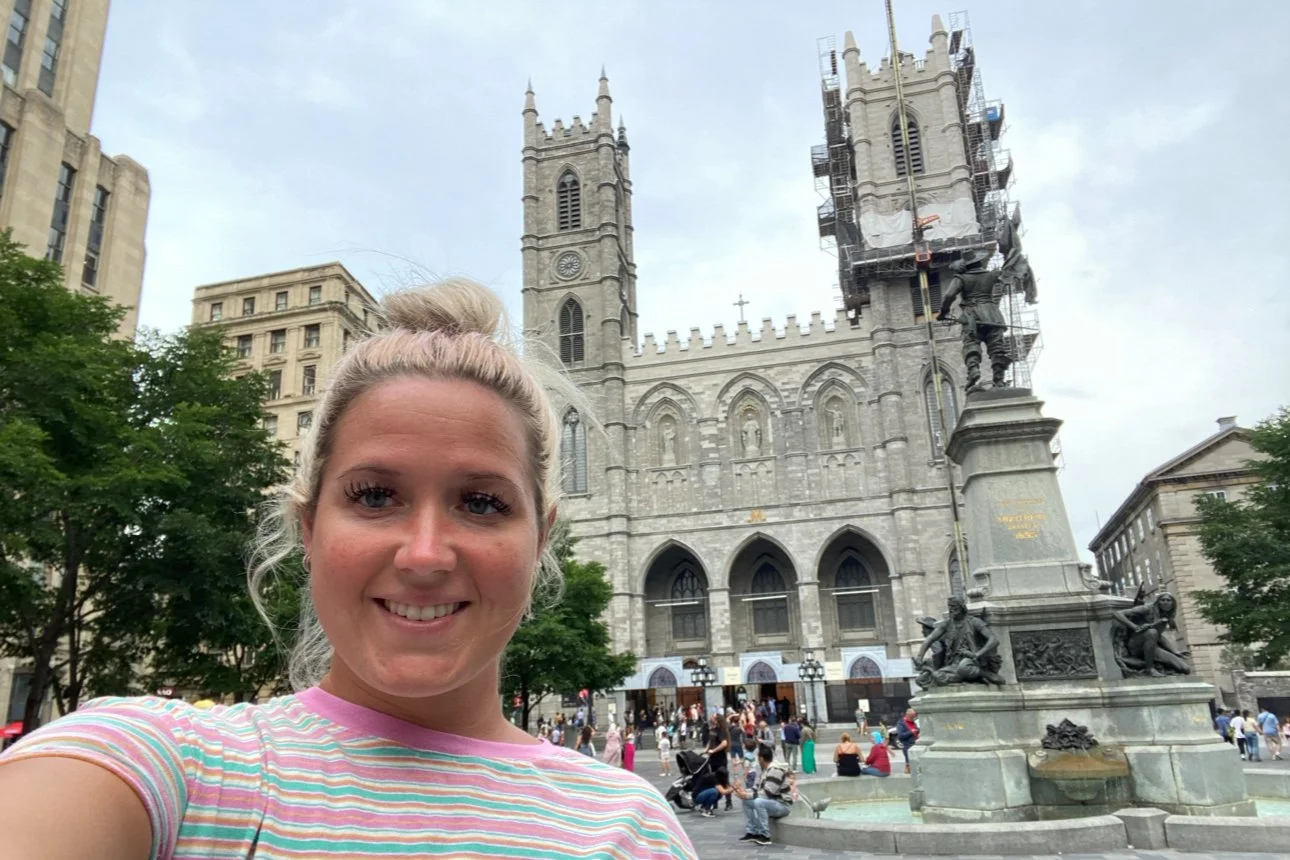 Woman taking a selfie in front of the illuminated Notre-Dame Basilica in Montreal, capturing the cathedral’s detailed Gothic Revival façade in the background.