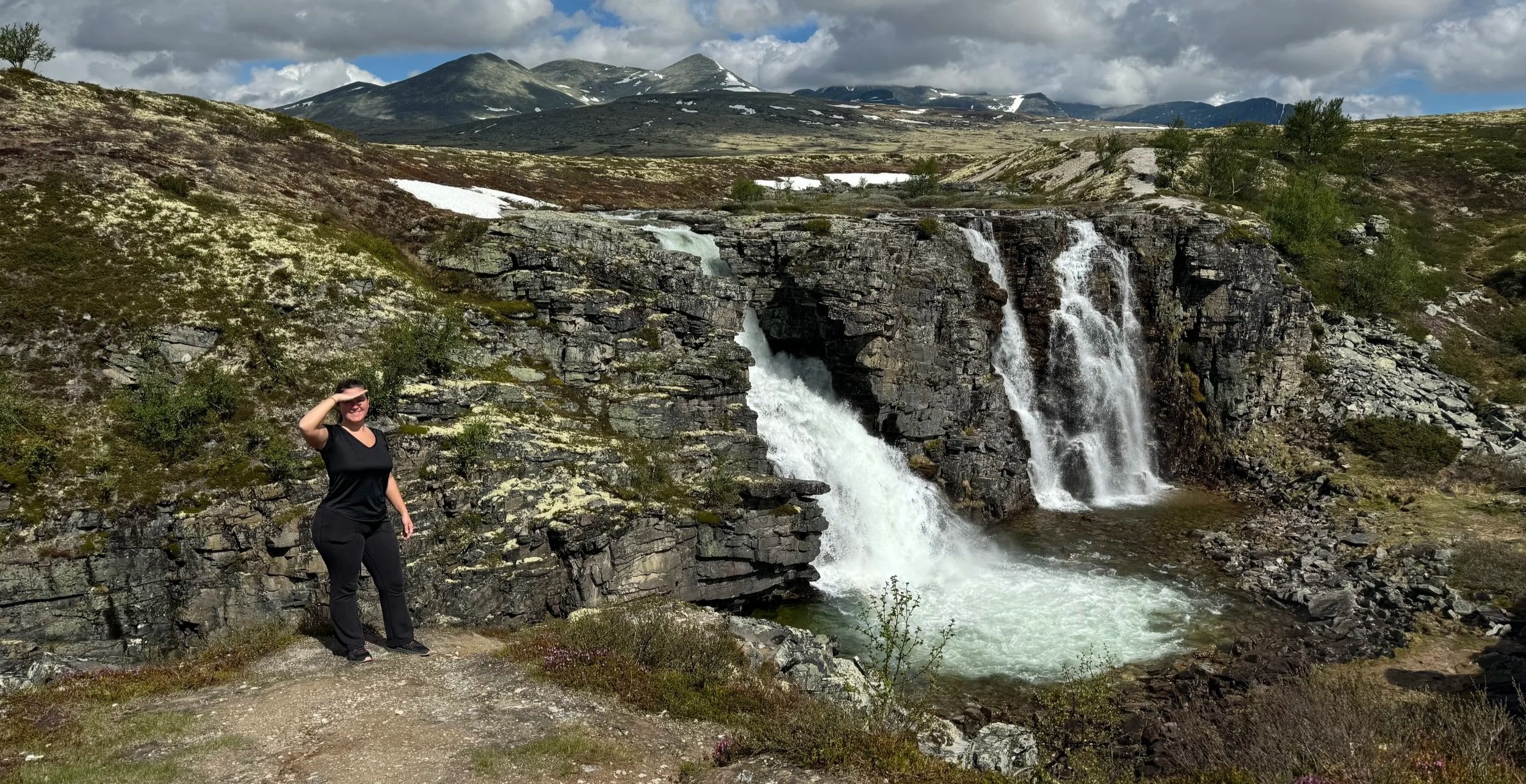 Woman smiling in front of a large waterfall surrounded by a few smaller cascades, lush natural landscape in the background Storulfossen to Spranget Loop Hike