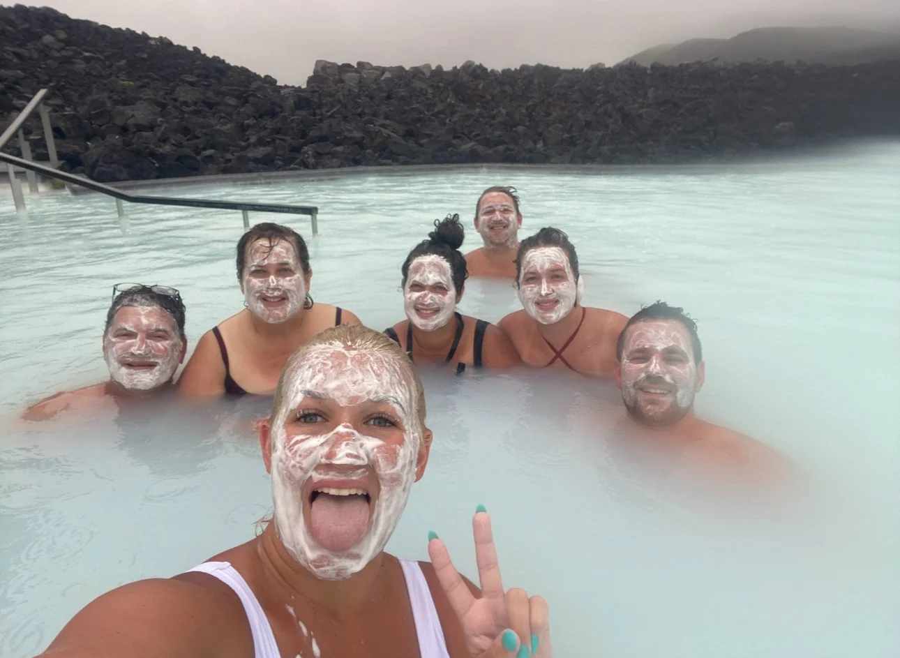 Family smiling together in the Blue Lagoon with white silica mud on their faces.