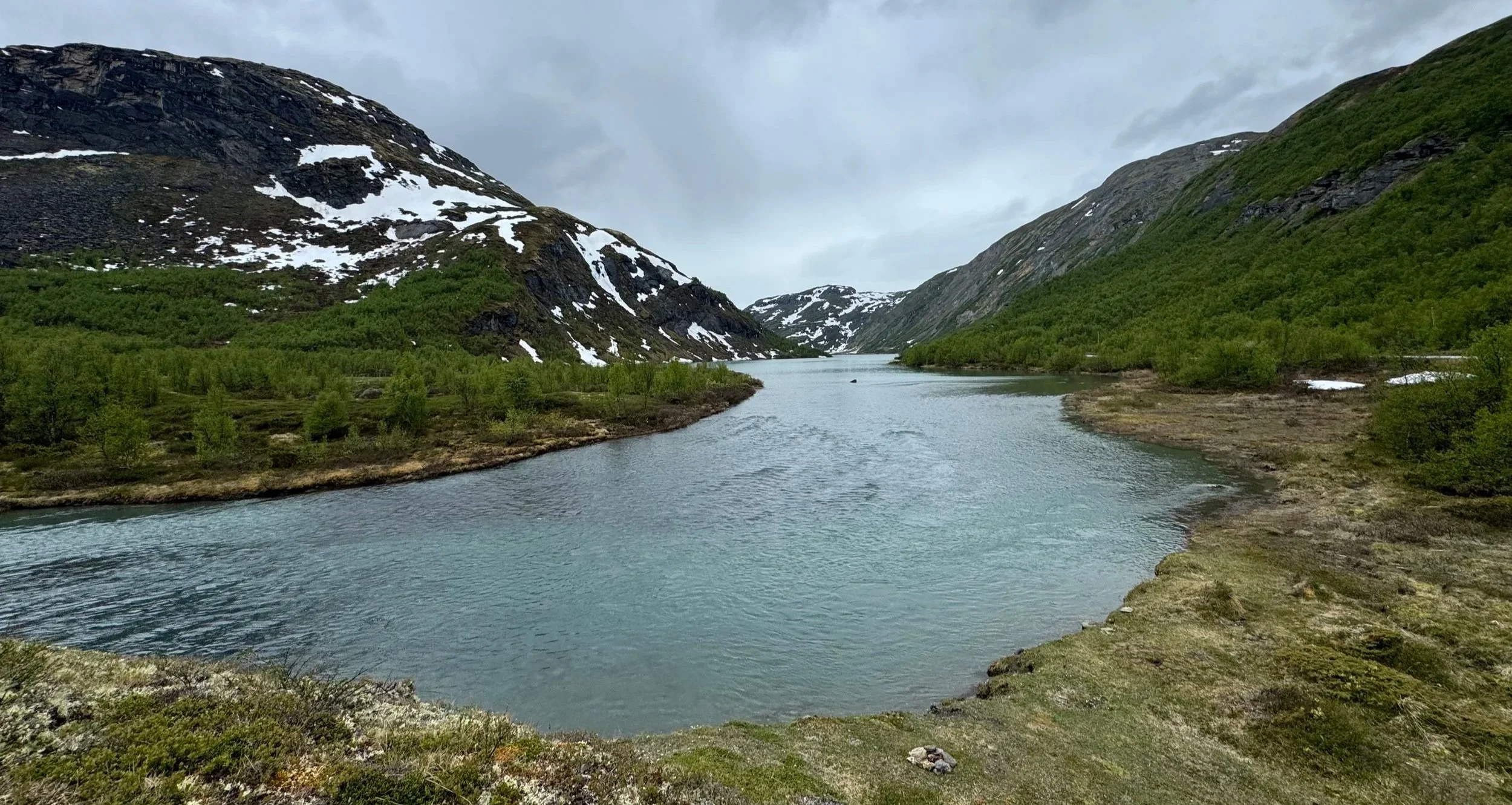 Scenic fjord with hills and snow-covered mountains in the background, calm Arctic waters reflecting the landscape in Norway