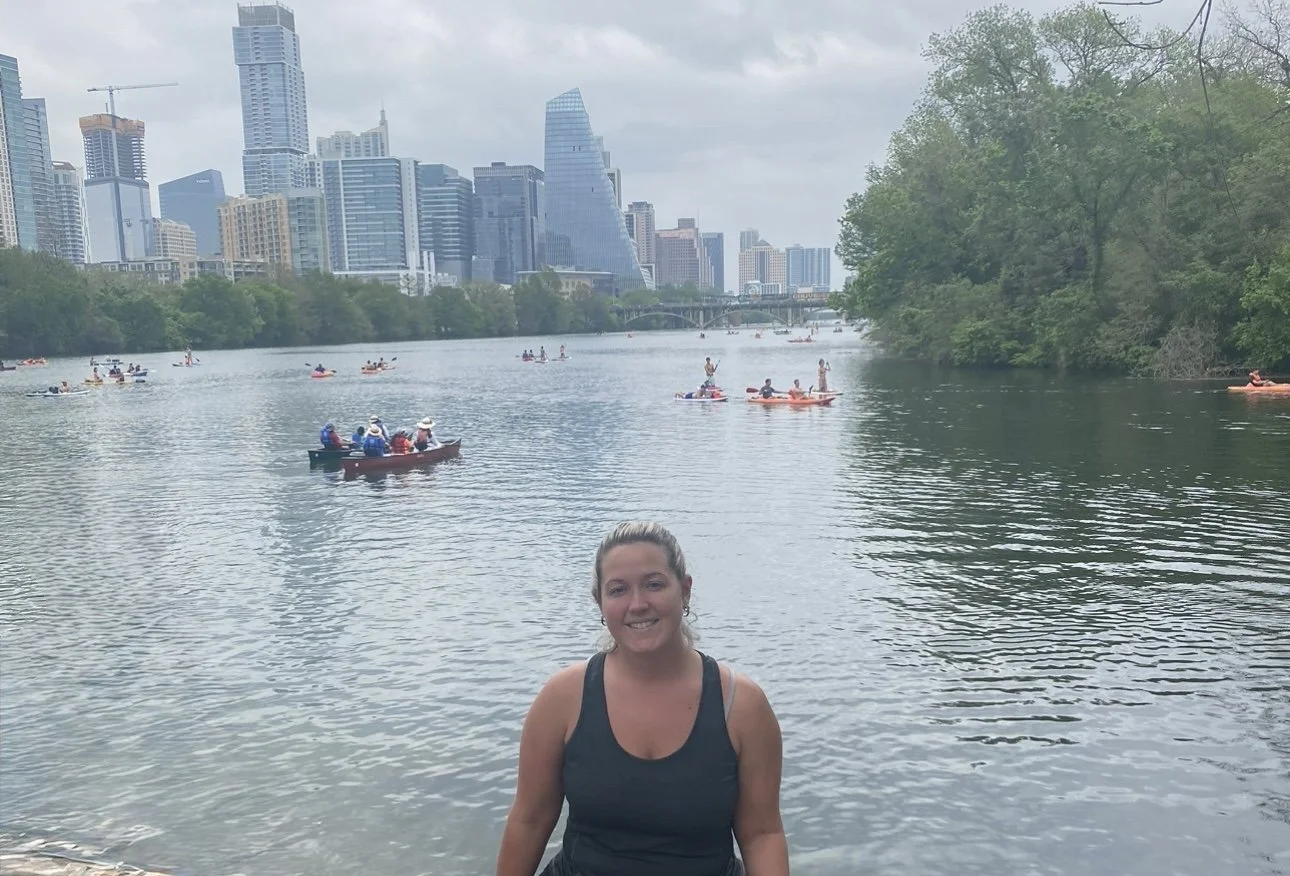 Girl smiling in front of a river at Zilker Metropolitan Park in Austin, Texas, with cityscape and park scenery in the background.