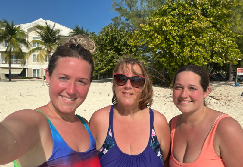 Selfie of a mom and two sisters smiling together on a sunny beach.