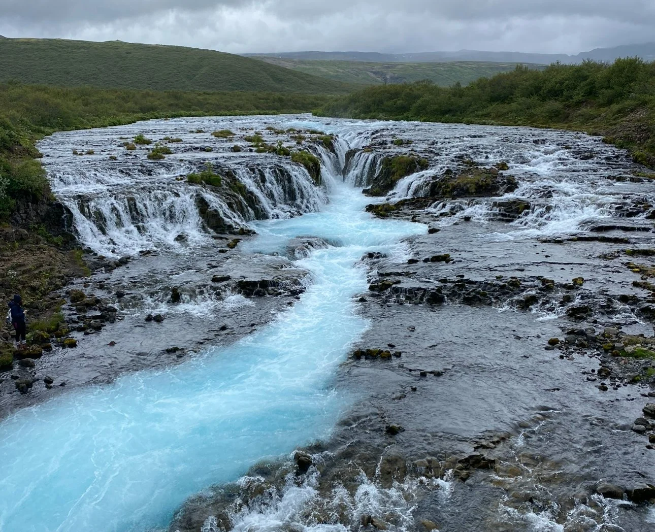 The cascading turquoise waterfalls of Bruarfoss in Iceland surrounded by rocky terrain.