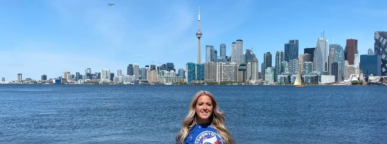 Smiling woman posing on Ward’s Island in Toronto Island Park with the city skyline visible across the water.