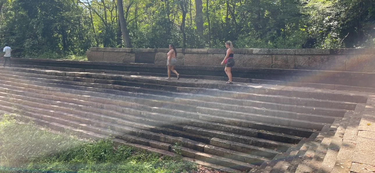 Two people walking along the ancient stone stairs at Ritigala Archaeological Reserve in Sri Lanka.