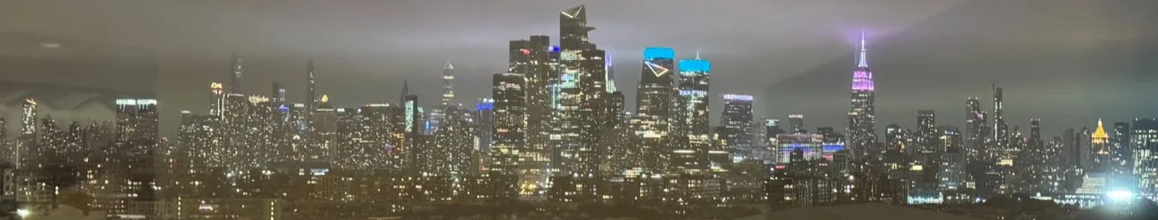 The New York City skyline illuminated at night with city lights shining in the sky.