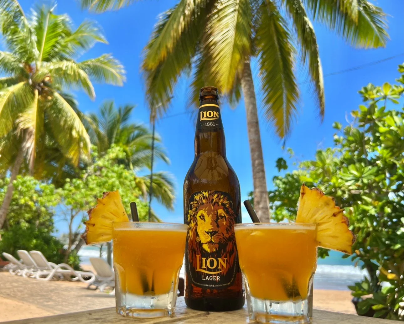 Lion Lager beer placed between two colorful fruity cocktails at Paradise Beach Club.