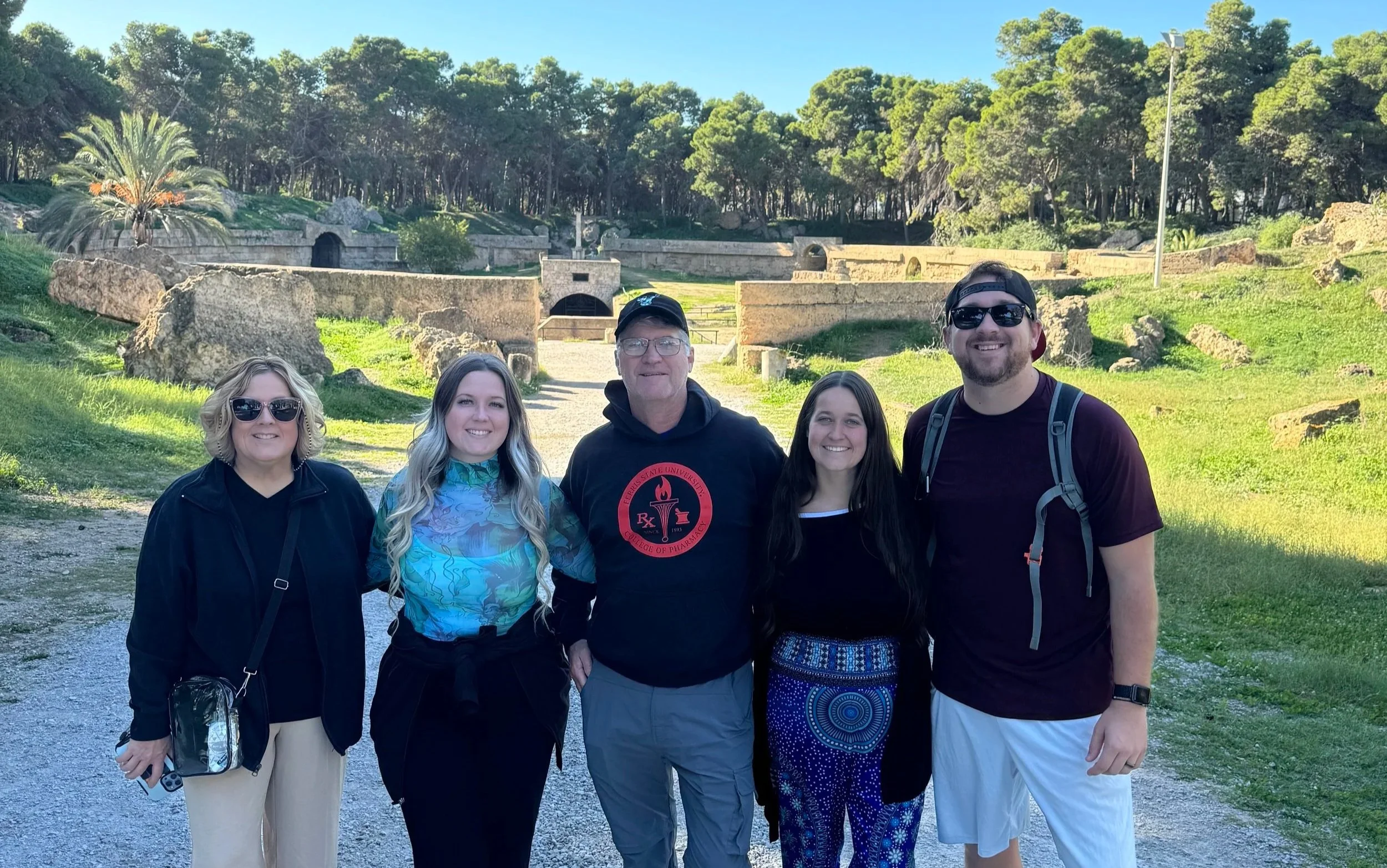 A family standing in front of the ancient Roman Amphitheater of Carthage in Tunisia, smiling with historic stone ruins behind them.