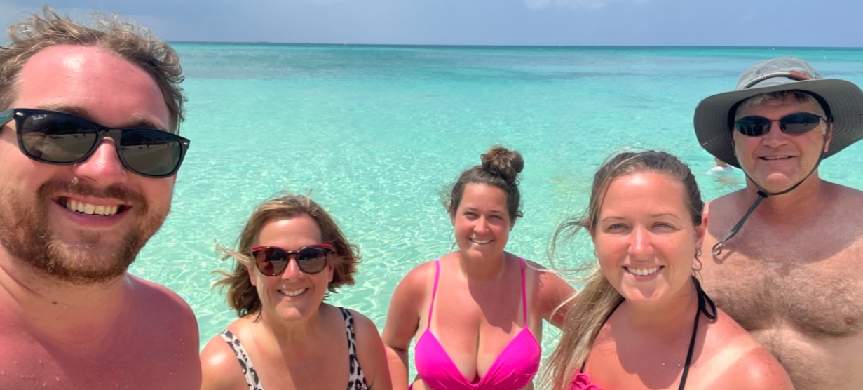 Family smiling together for a selfie in front of crystal-clear turquoise water.