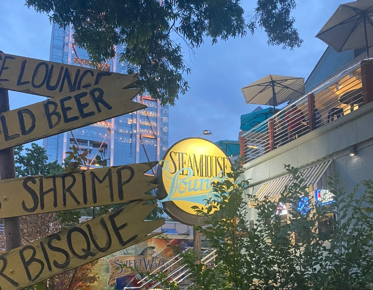 Exterior of Steamhouse Lounge featuring bright yellow food signs in front of a city view.