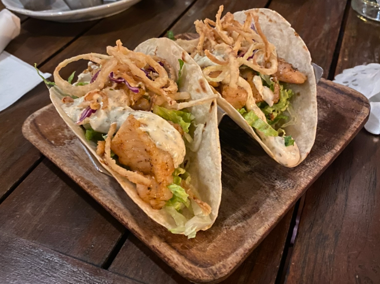 Two lionfish tacos topped with fresh ingredients and drizzled with sauce.