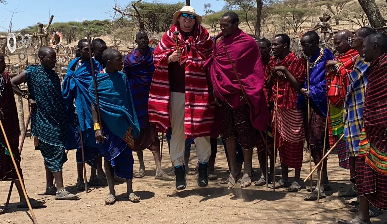 Man jumping alongside members of the Maasai tribe in Kenya during a traditional celebration.