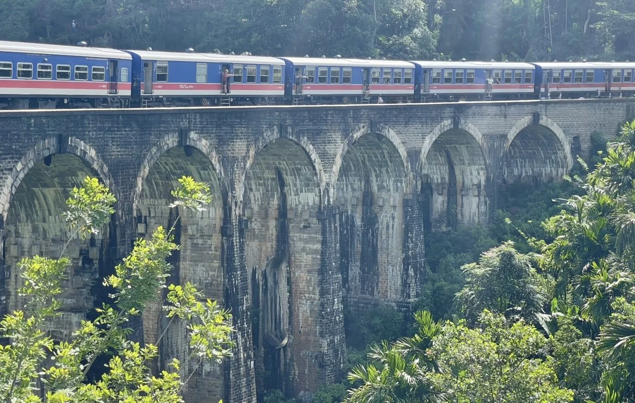 View of the Nine Arch Bridge in Sri Lanka with two girls smiling in the distance.